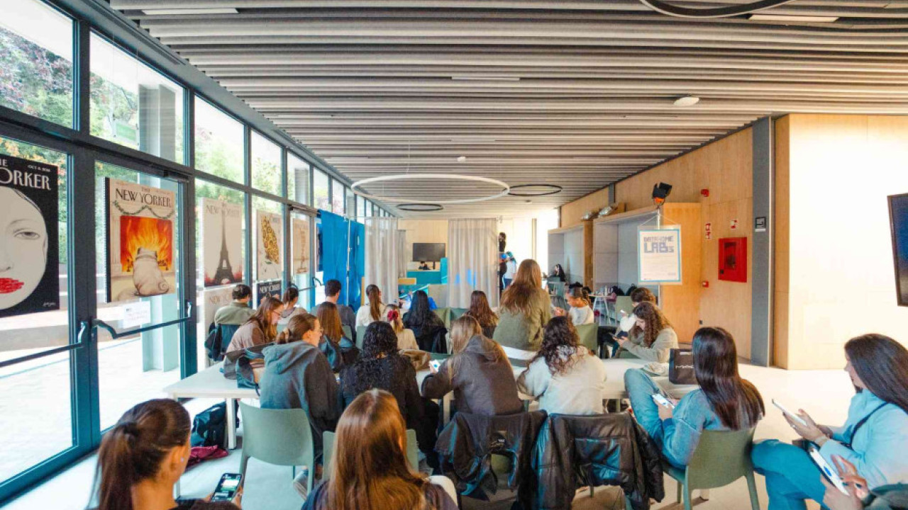 Un grupo de jóvenes está sentado en una sala luminosa escuchando una charla, participando en DataHomeLab: La estancia del futuro II, un taller interactivo sobre IA generativa aplicada al diseño.